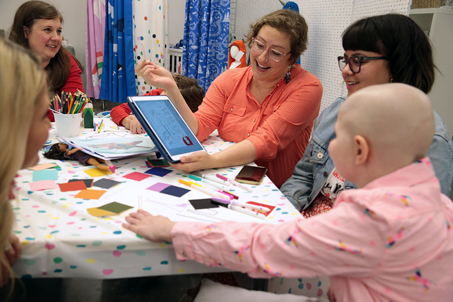 Hallie and four designers sit around a table, looking at designs on a digital tablet and smiling