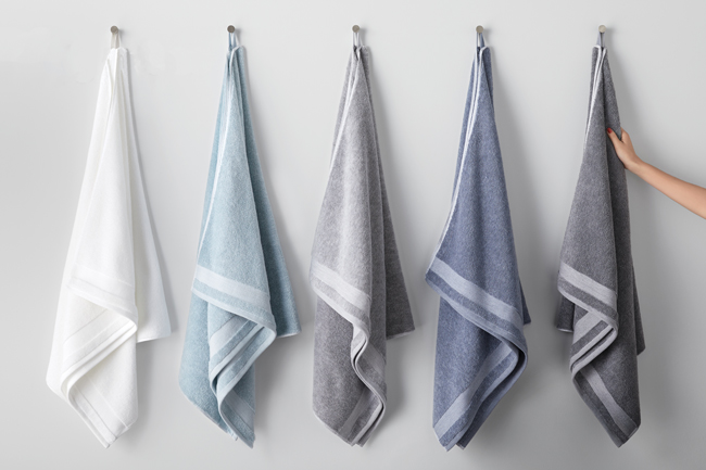 Five towels in white and shades of blue and grey hang from loops in a row