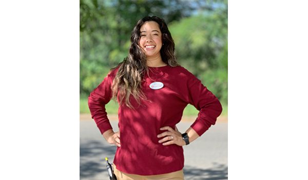 Melanie stands outside smiling with her hands on her hips. She's wearing red and khaki and a Target name badge and walkie-talkie, and has long, black hair.