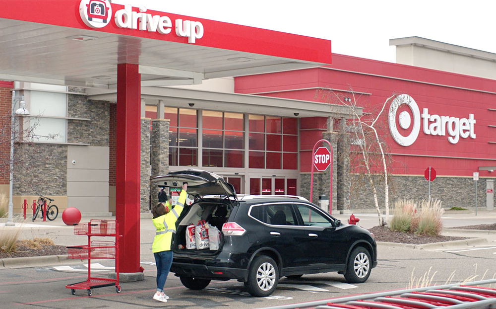 At the Drive Up lane in front of a Target store, a team member in a yellow vest places an order in the back of a guest's vehicle