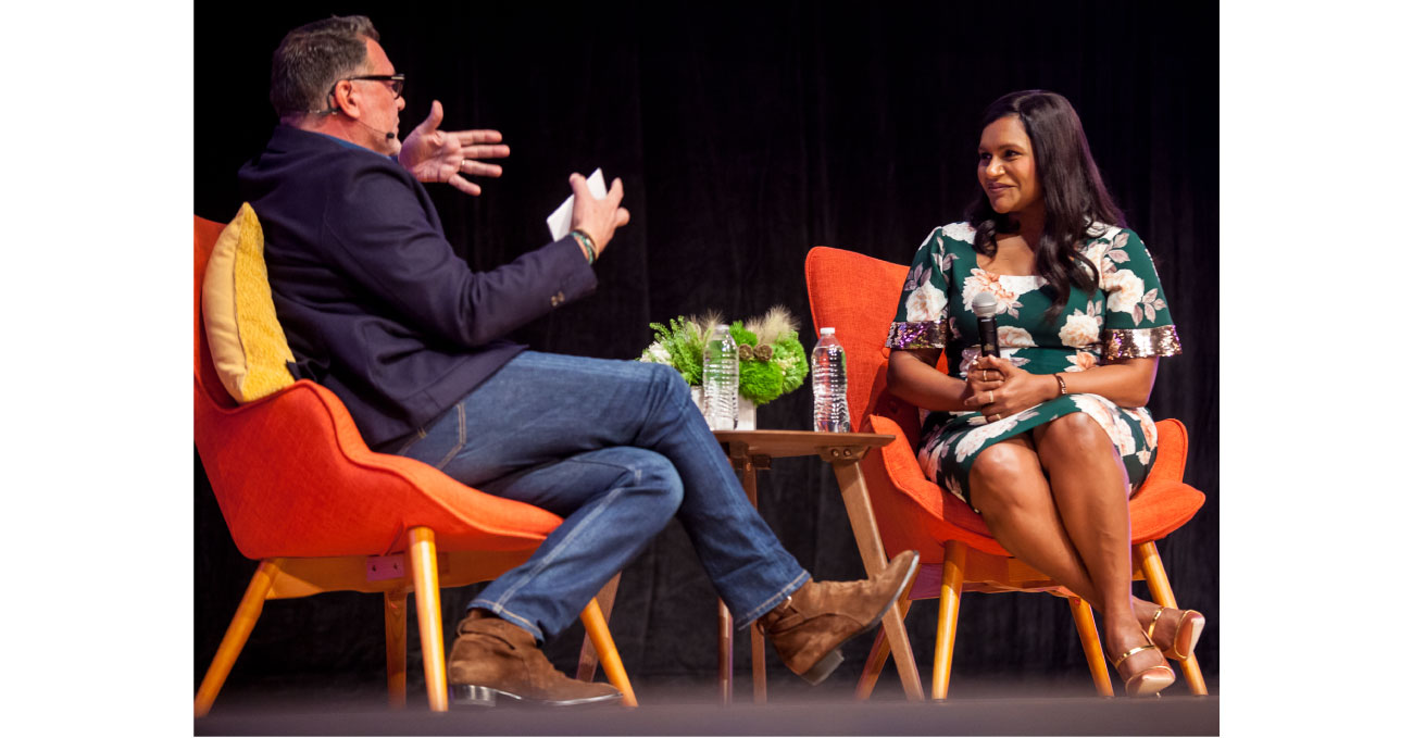 Mark Tritton and Mindy Kaling sit in orange chairs having a conversation on stage