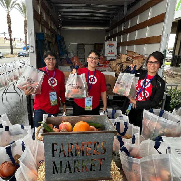 Target team members holding up shopping bags behind a sign that reads "farmers market."
