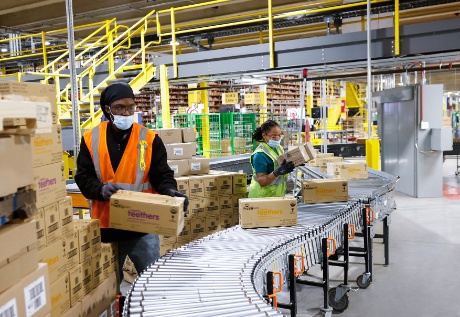 Two team members wearing vests place boxes onto a conveyor.