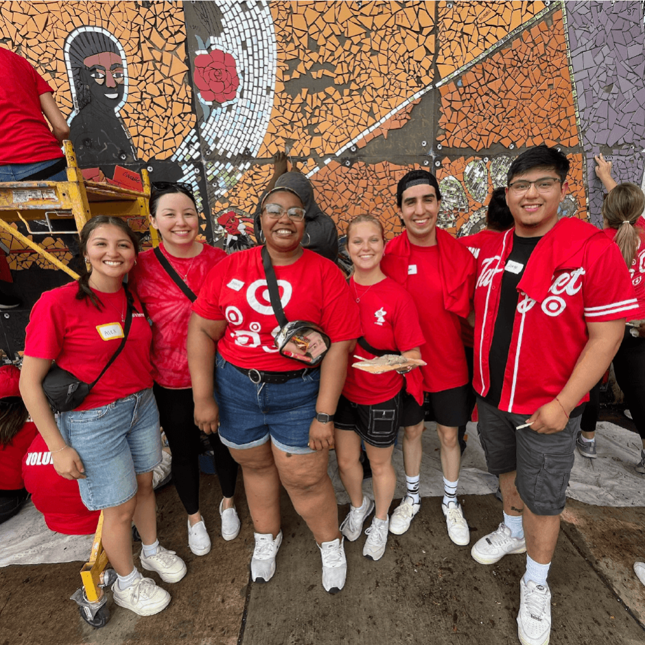 A group of people in Target shirts stand in front of a mural smiling.