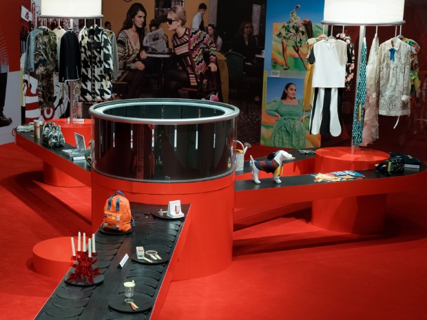 Hero image with the text “Guest Experience: Inside Target’s Next Chapter of Great Design for All” beside a vivid red Target by Design exhibit at New York City’s New Museum, featuring circular display structures, a long black platform lined with curated objects, fashion imagery and colorful products throughout the space.