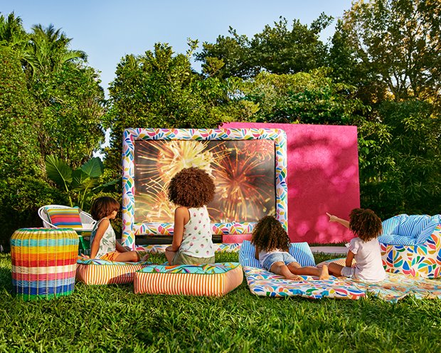 a group of children sitting on colorful cushions in a grassy area