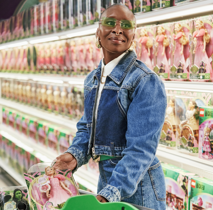 Cynthia Erivo poses with a green shopping cart in an aisle of Wicked dolls.