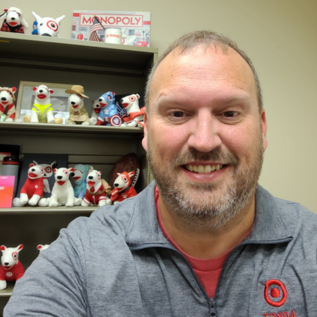Steve smiles while sitting in front of a bookshelf filled with Target plush dogs.