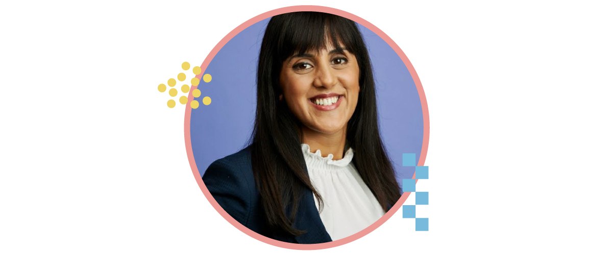 A photo of a smiling team member with brunette hair, donning a blue blazer and a formal white shirt.