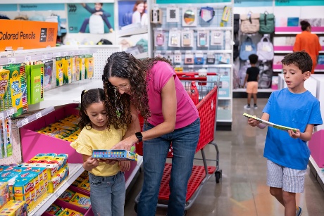 A parent shops with their children, reading packaging information aloud to one of them.