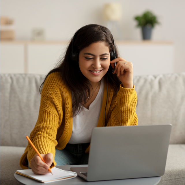 A person in a yellow sweater sits while working at a laptop.