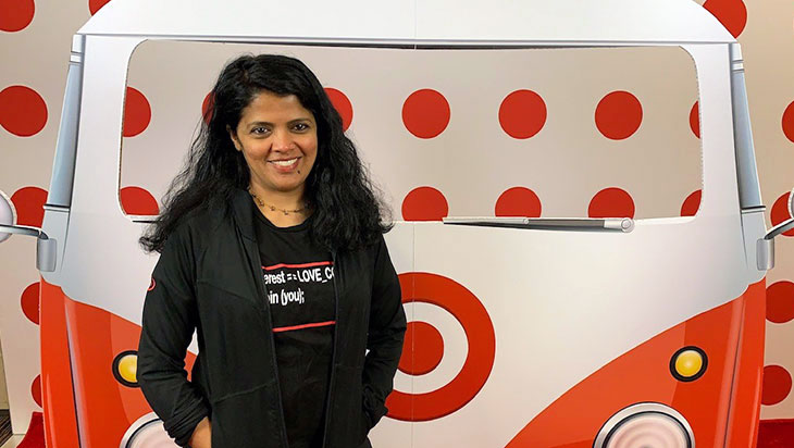 an Indian woman stands in front of a photo backdrop with a bus and bullseye logos