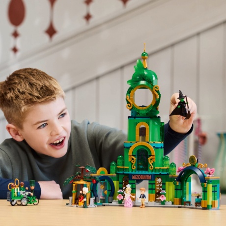 A boy plays with a LEGO set that resembles the Emerald City from Wicked.