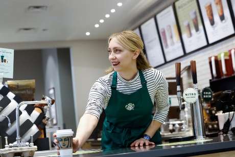 A Starbucks barista smiles and places a beverage on the counter.