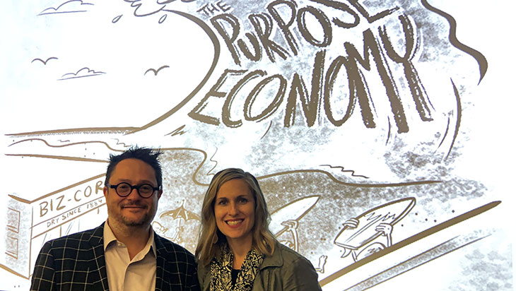 a man and woman stand in front of a graphic with "the purpose economy"