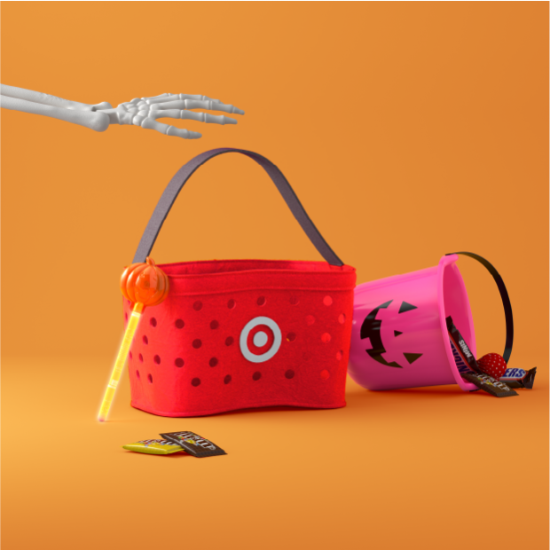 A skeleton arm reaching for a red Target shopping basket and a pink Halloween bucket laying on its side with candy spilling out of it.