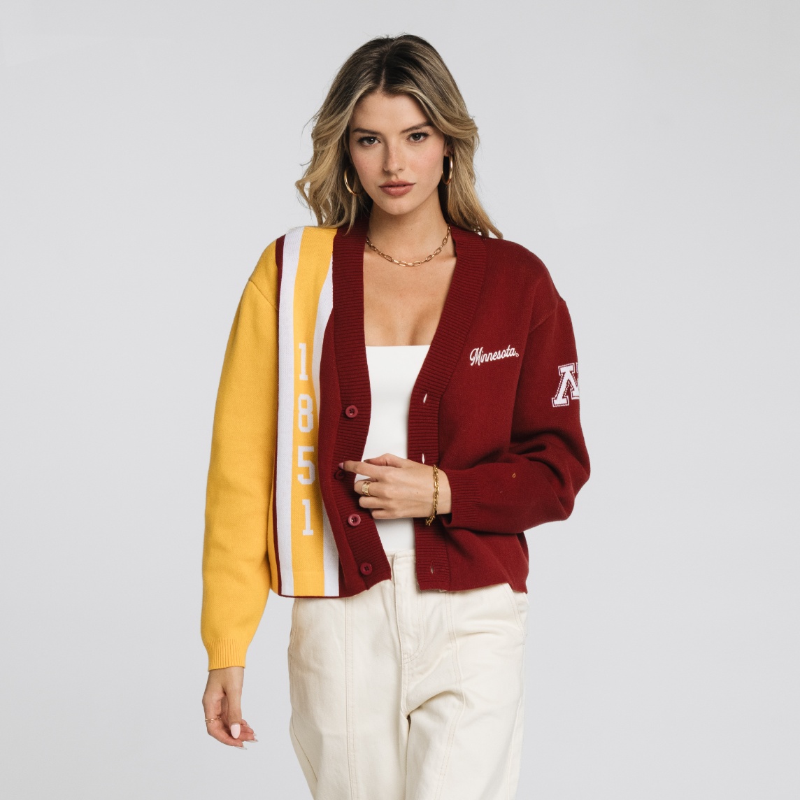 A person wearing a maroon and gold cardigan with “1851” and “Minnesota” lettering poses against a plain background, styled with a white top and cream pants.