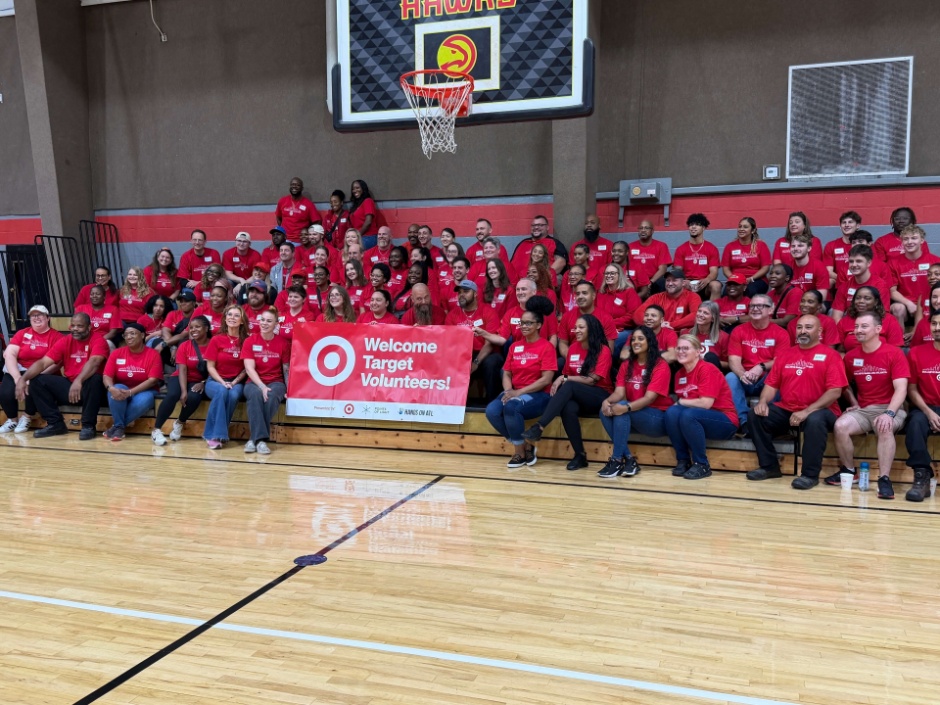 A group of Target team member volunteers sit on bleachers in a gym surrounding a banner that says welcome Target volunteers.