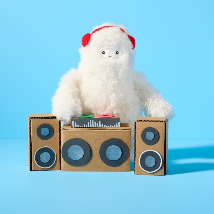a plush Get-Ready Yeti standing behind a stereo system made out of paper and cardboard boxes